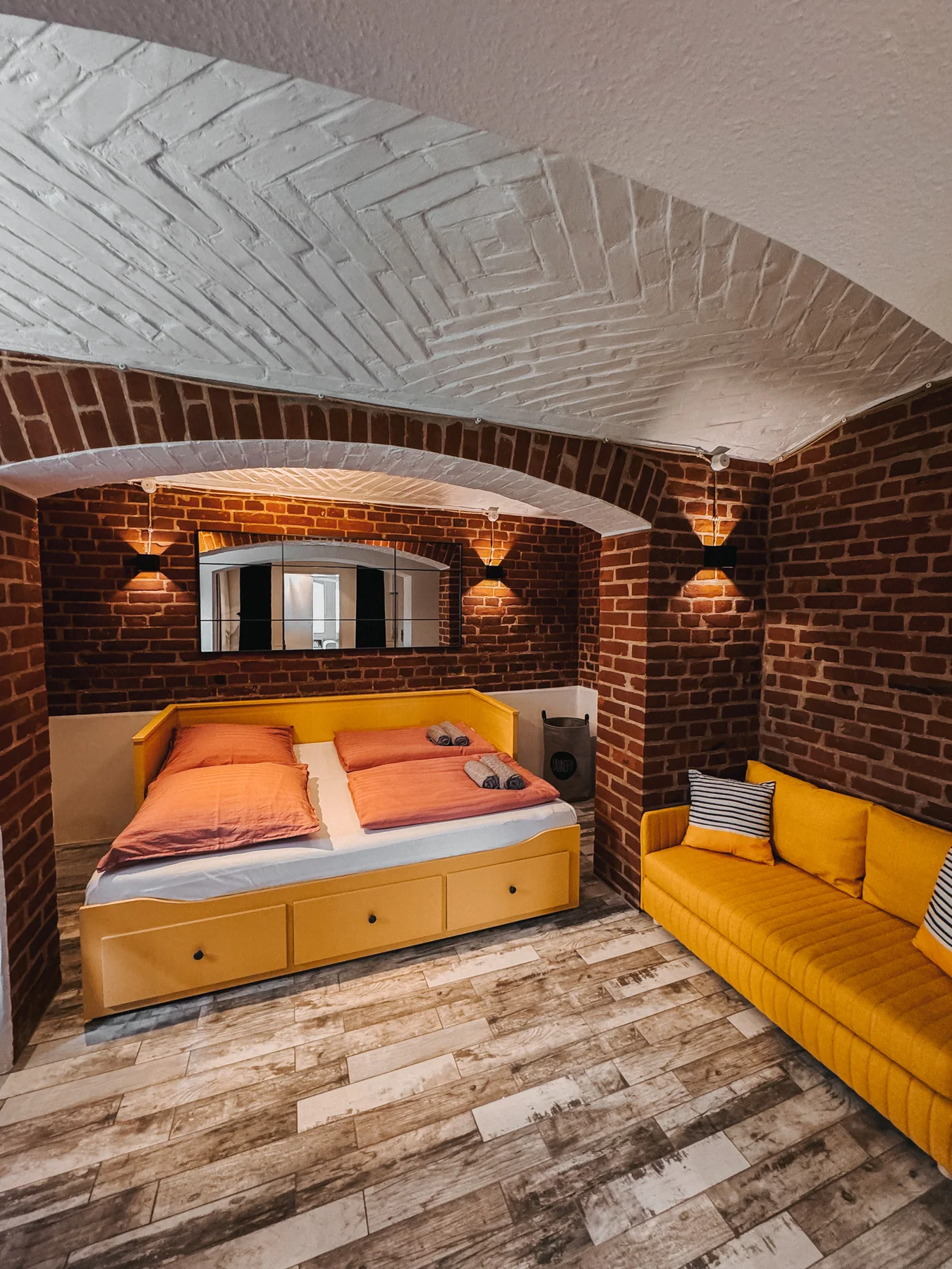 Weite Gesamtansicht mit Bett, Sofa und Backsteingewölbe